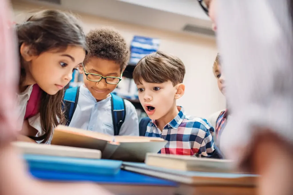 A group of young students looking at books on a table.