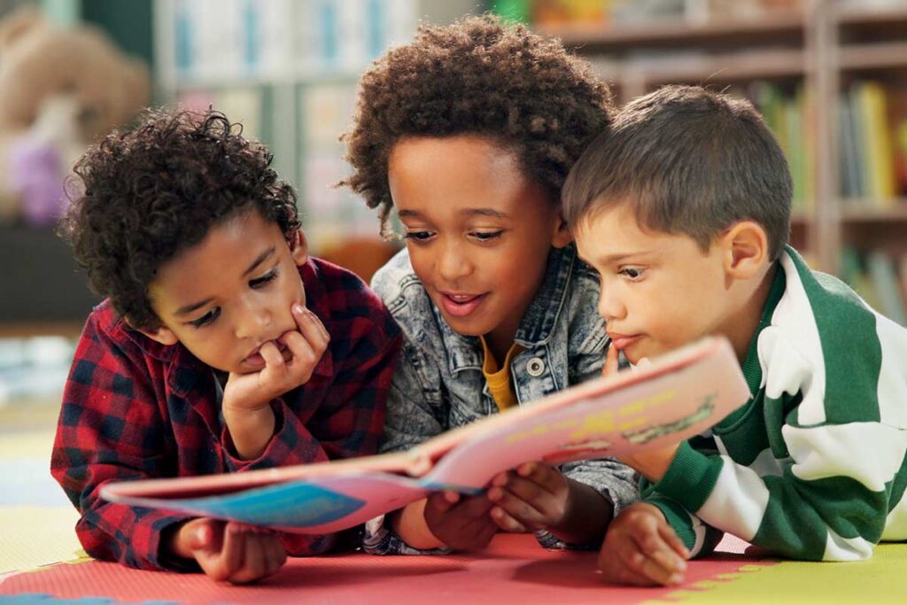 Three children reading a book together on the floor.