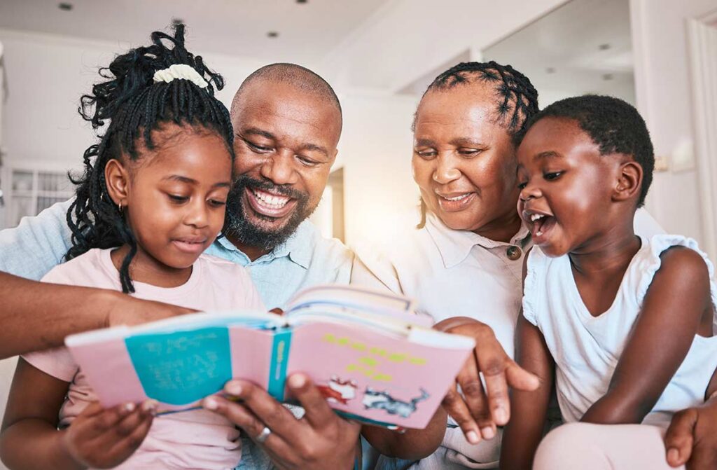 Two young children reading a book with their grandparents.